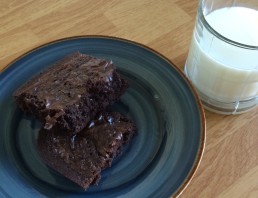 two brownies on a blue plate with a glass of milk